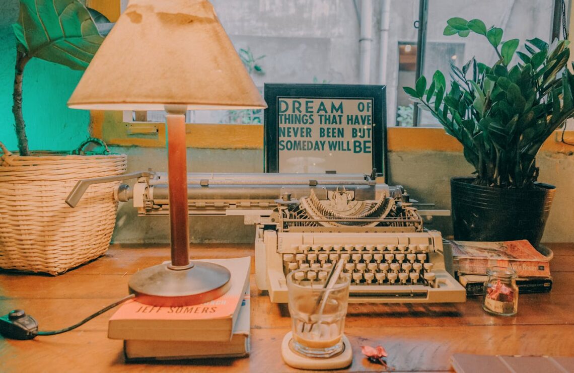 Cozy minimalist desk with a vintage typewriter, warm lamp, plants, and framed inspirational quote.