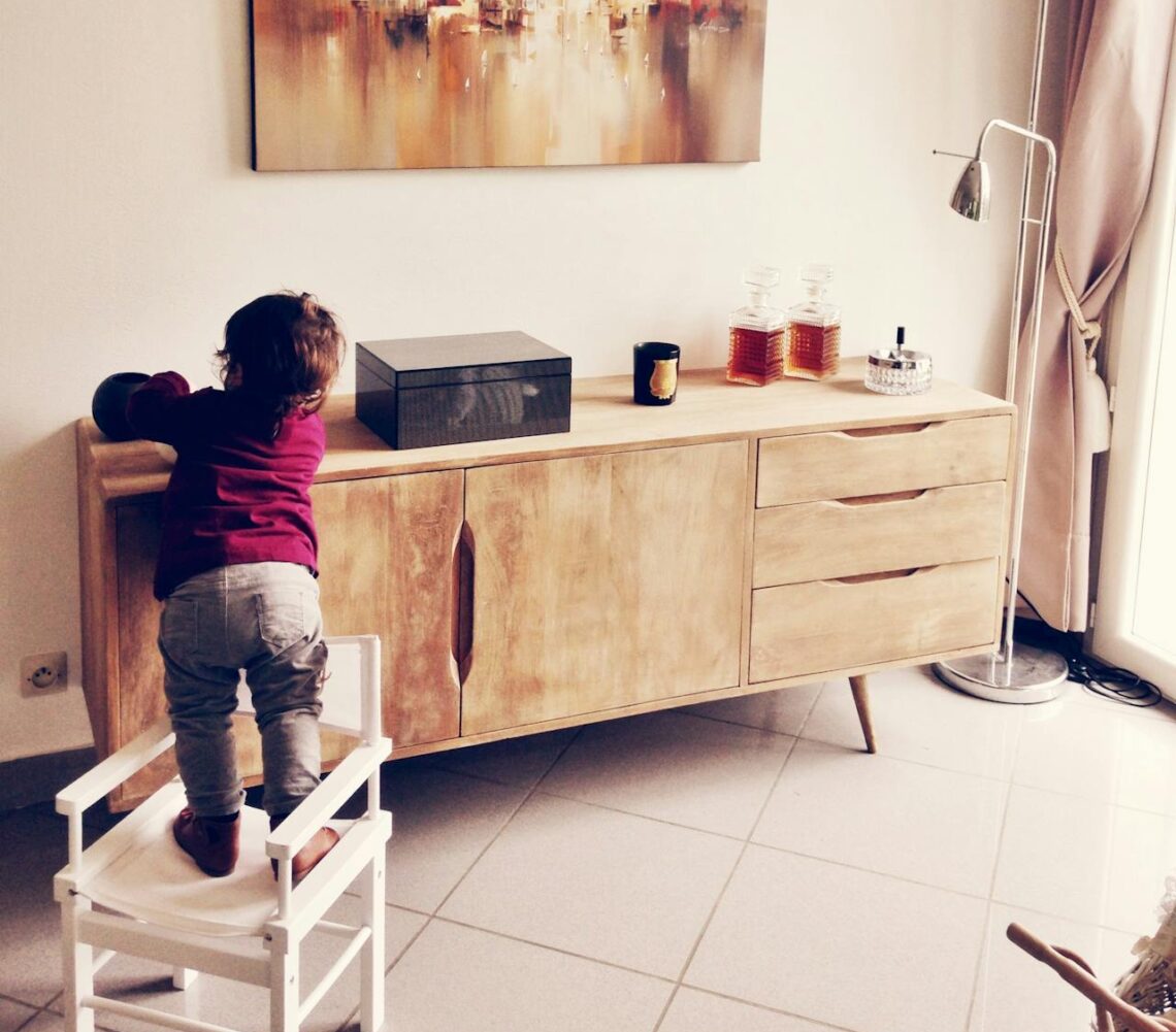 toddler-standing-on-white-chair-beside-sideboard